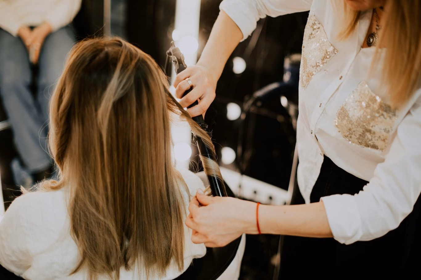 Stylistin formt mit dem Lockenstab eine Welle in langes, blondes Haar